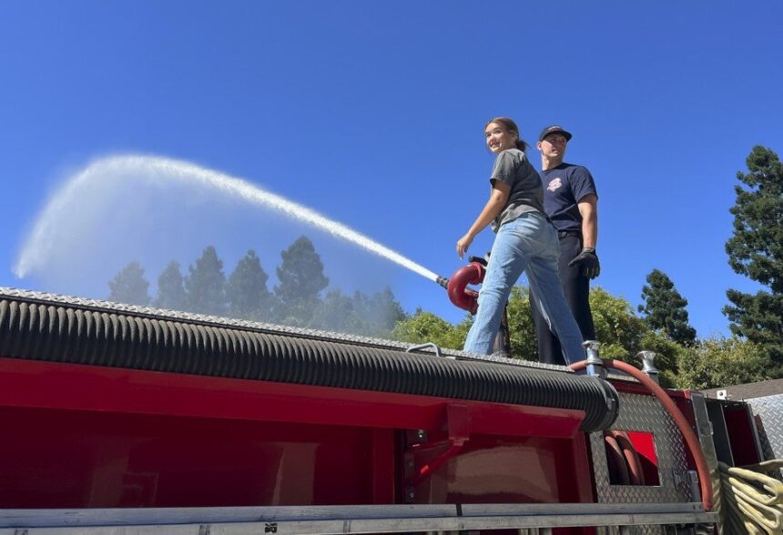 Fire and Emergency Services teacher with student sparying water off firetruck