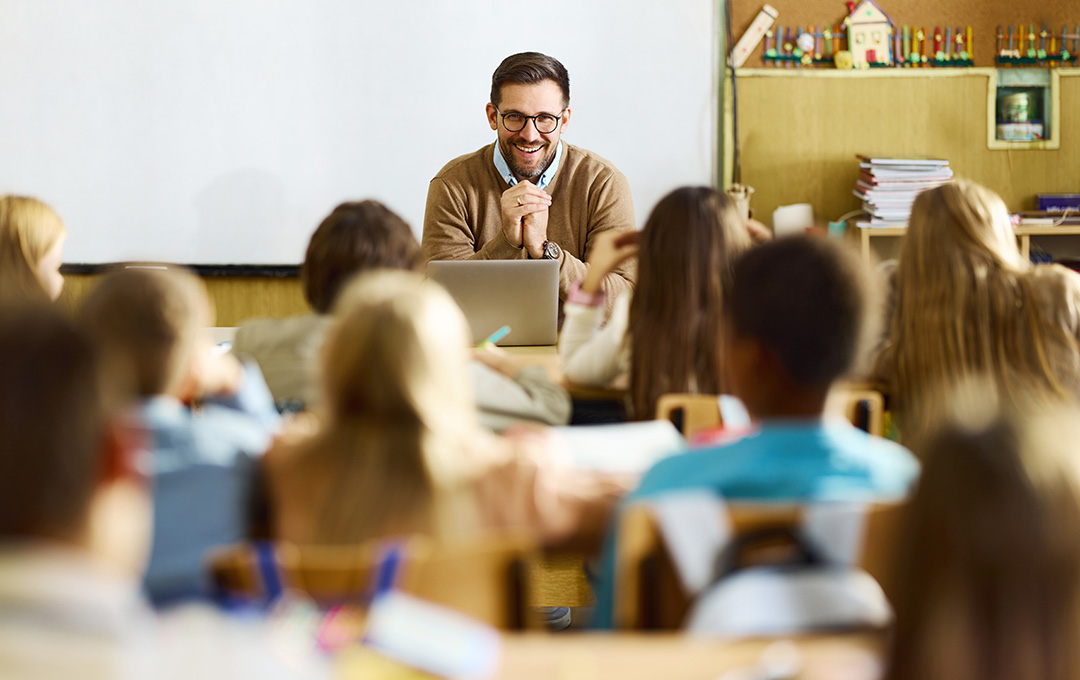 Happy male teacher giving a lecture to his elementary students during a class in the classroom.
