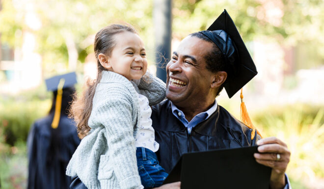 student in graduation gown holding a child