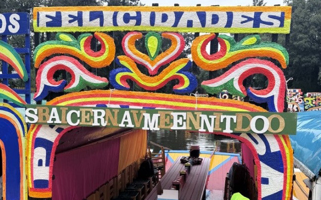 Colorfully Decorated Trajinera Boat With An Ornate Painted Arch And Covered Seating On A Canal.