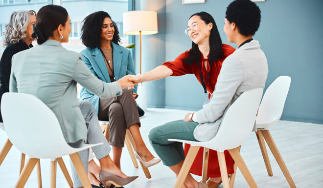A group of professionals seated in a circle shake hands during a collaborative meeting in a modern office.