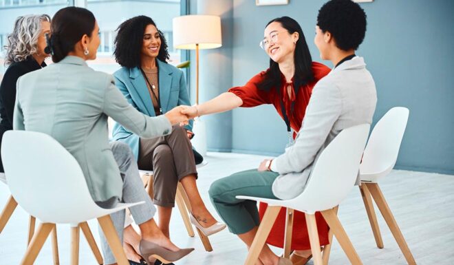 A group of professionals seated in a circle shake hands during a collaborative meeting in a modern office.