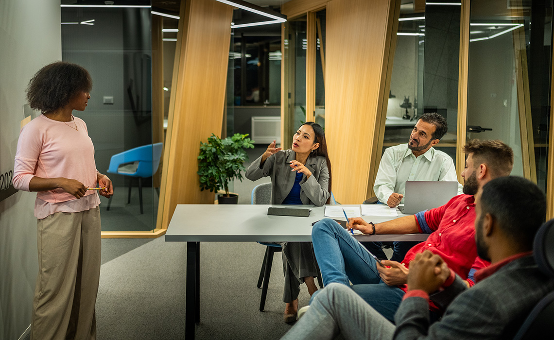 Young Businesswoman Presenting To Diverse Team In Modern Office Setting