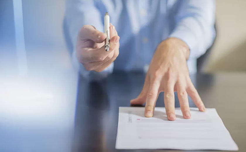 Person holding a pen over a document on a table