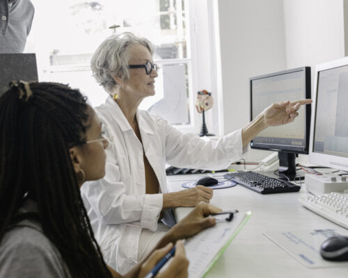 Healthcare Professional Points To Information On A Computer Screen While A Student Takes Notes