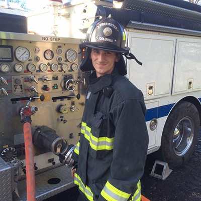 Stewart Wearing Firefighter Gear While Standing Beside A Fire Engine.